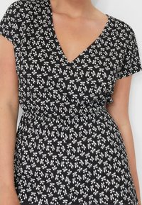 Sort kjole med et hvidt blomstermønster, korte ærmer og v-hals design. Materialet ser tekstureret og letvægtigt ud. Samlet talje detalje.