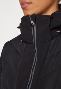 Gros plan sur une personne portant une veste noire matelassée avec un col montant et une fermeture éclair avant visible.