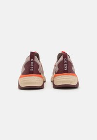 Adidași sport dintr-un material gri deschis, cu accente burgundy închise, tălpi texturate, detalii portocalii strălucitoare și logo-ul „GUESS” pe călcâi.