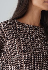 Brauner Stoffoberteil mit rundem Ausschnitt, das ein geometrisches Muster aus schwarzen, weißen und cremefarbenen Punkten aufweist. Weicher Stoff mit lockerer Passform.