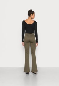 Camisola preta de mangas longas com um decote profundo nas costas e calças verdes-oliva largas, combinadas com sapatos de salto alto pretos. Textura suave, forma ajustada.
