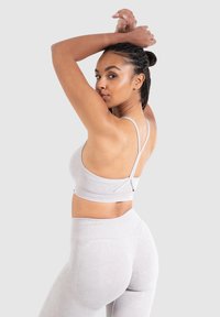 Ljust grå sport-bh med tunna axelband och bandad nederkant; kombinerad med matchande högmidjade leggings med en texturerad design.