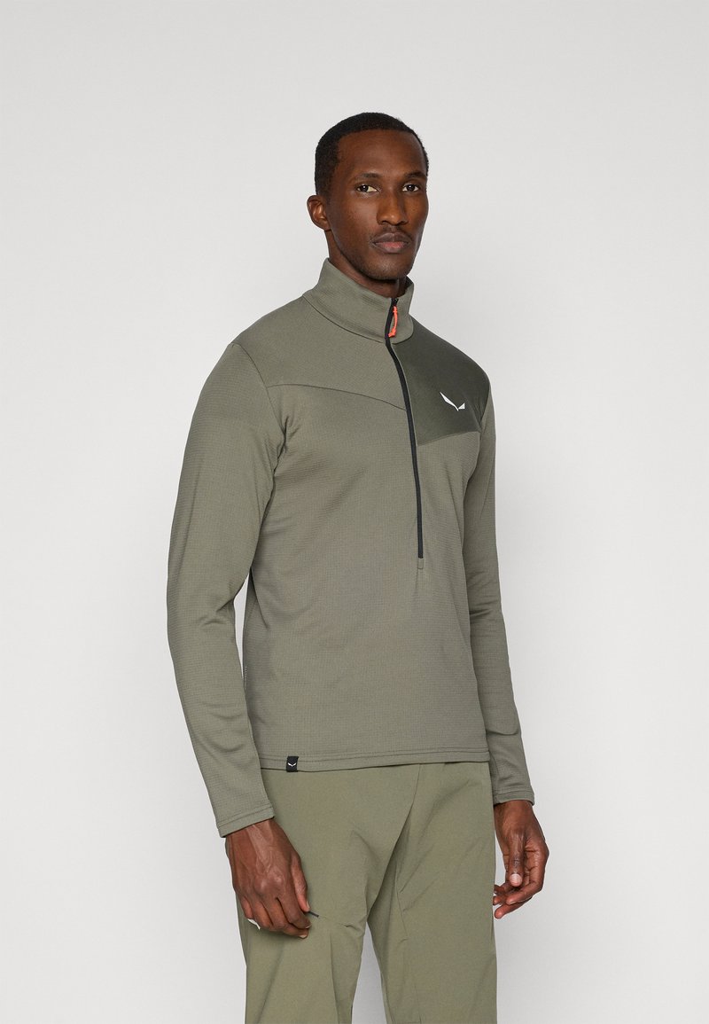 Olivgrüner Zip-Pullover aus strukturiertem Stoff; verfügt über einen hohen Kragen, ein schwarzes Paneel mit Logo und einen orangefarbenen Reißverschlussakzent.