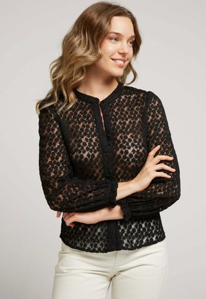 Blouse en dentelle noire avec un col rond, présentant de longues manches bouffantes et des motifs floraux. Le design comprend un devant boutonné et un tissu texturé.