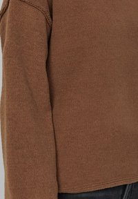 Brauner Strickpullover mit Rippenstruktur, langen Ärmeln und legerer Passform. Beinhaltet dezente Nähte entlang der Nähte.