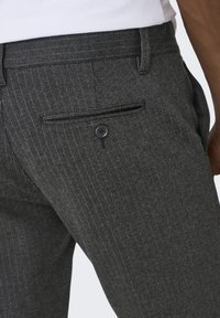 Pantalones grises texturizados que presentan un sutil patrón de rayas, con un bolsillo trasero único y un pequeño cierre de botón negro.