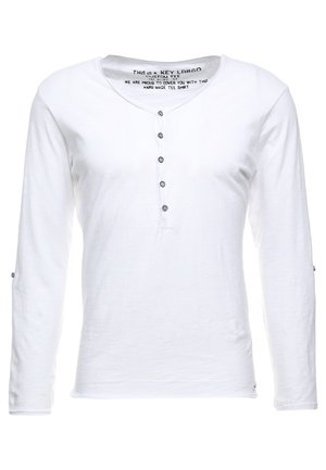 Camisa blanca de manga larga fabricada en tejido ligero, con un escote tipo henley, seis botones azules y detalles de costura sutiles.