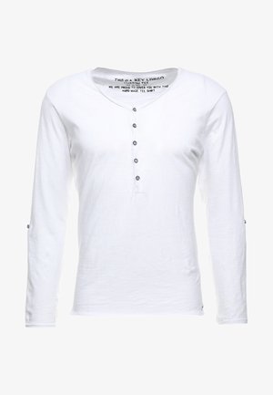 Camisa blanca de manga larga fabricada en tejido ligero, con un escote tipo henley, seis botones azules y detalles de costura sutiles.