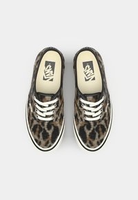 Leopard print slip-on shoes with white laces, black trim, and a rubber sole. The interior features a beige insole with a Vans logo.