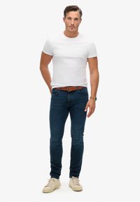T-shirt blanche ajustée, jeans en denim bleu, ceinture en cuir marron et baskets beiges. Design simple sans motifs ; texture lisse.
