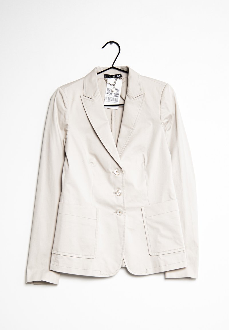 Light beige fitted blazer with a single-breasted design, three button closures, two front pockets, and subtle stitching details.