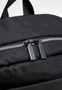 Černý batoh s dvojitým zipovým uzávěrem, vybavený kovovými stříbrnými zuby zipu a látkovými taháčky se znakem "U.S. Polo Assn.". Texturovaný materiál.