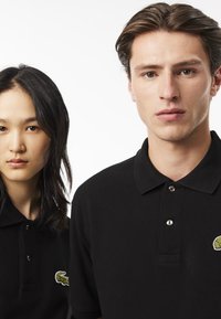 Des polos noirs en coton texturé, avec un logo de crocodile vert brodé sur la poitrine gauche et deux patins à boutons.