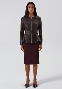Giacca peplum in pelle marrone con vita cinturata, chiusura con zip e maniche corte, abbinata a una gonna a tubino bordeaux aderente.