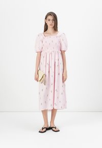 Roza midi obleka s napihnjenimi rokavi, nabrano telo, cvetlični vzorci in stranski razporek. Skombinirana z zlatim usnjenim etuijem in črnimi sandali.