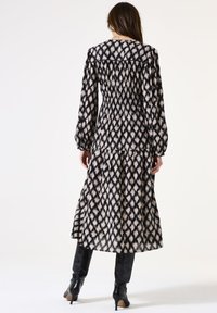 Robe à manches longues avec un motif géométrique noir et crème, taille élastique et jupe fluide. Fabriquée en tissu léger.