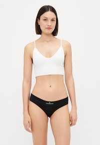 Bralet alb, ajustat, cu un design în formă de V; asortat cu chiloți bikini negri, cu un logo pe banda de talie. Textură de țesătură netedă.