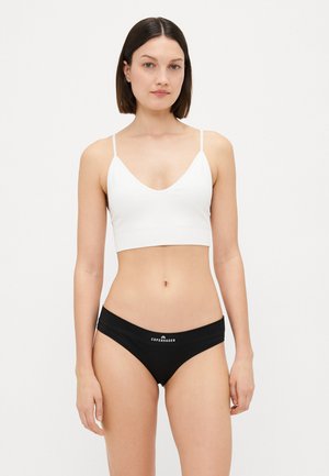Weißer, taillierter Bralette mit V-Ausschnitt; kombiniert mit schwarzem Bikiniunterwäsche mit Logo am Bund. Glatter Stoff.