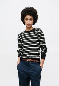 Πουλόβερ με μαύρες και άσπρες ρίγες, ριμπ υφή και στρογγυλή λαιμόκοψη, σε συνδυασμό με ναυτικά μπλε παντελόνια και καφέ ζώνη με στρογγυλή αγκράφα.