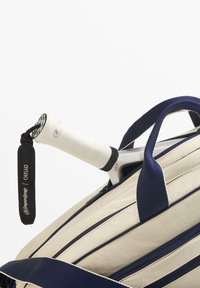 Tennislaukku kermanvärisenä laivastonsinisillä raidoilla, jossa valkoinen kahva ja sisällä näkyvä otelinja. Mukana musta merkitty hihna logolla.