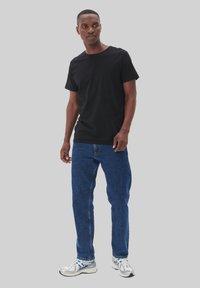 Tricou din bumbac negru cu guler rotund, asortat cu blugi denim albaștri. Modelul poartă încălțăminte sport argintie cu detalii albastre.