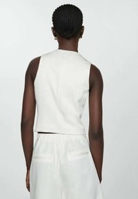Haut sans manches blanc avec un design cropped, associé à un pantalon blanc doté d'une taille élastique et de poches arrière, texture lisse.