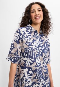 Bluse mit floralem Muster in Marineblau und Creme, kurze Ärmel, Knopfleiste, Leinenstruktur, mit aufgerollten Ärmeln und Brusttasche.