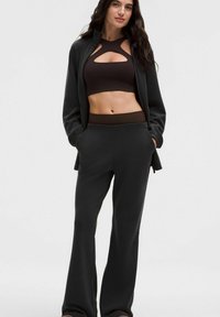 Čierna súprava na voľný čas s športovým topom s výstrihom, doplnená o pohodlné nohavice s voľným strihom. Materiál pôsobí mäkko a pružne.