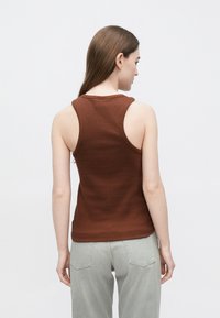 Brązowy bezrękawnik z prążkowanej bawełny, o dopasowanym kroju i szerokich pachach, zestawiony z jasnoszarymi jeansami.