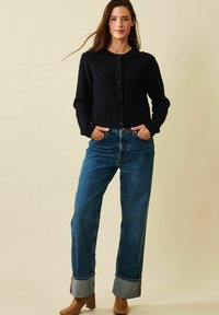 Marinblå kabelstickad cardigan med rund halsringning och knäppning, matchad med högmidjade blå raka jeans och bruna klackade ankle boots.