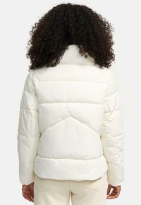Veste matelassée blanche avec un col montant, texture matelassée et sections rembourrées. Présente un design de renfort au dos et est fabriquée dans un matériau brillant.