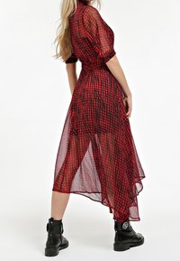 Robe transparente à carreaux rouge et noir avec un ourlet asymétrique, des manches bouffantes, une taille cintrée, portée avec des bottes de combat noires à lacets.