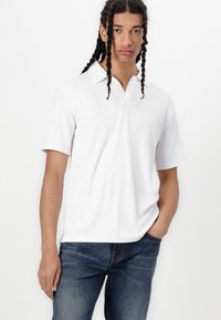 Vit kortärmad polo t-shirt med en strukturerad vågmönster och krage, i kombination med blåa jeans.