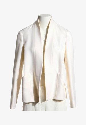 Blazer de color crema con abertura frontal, mangas largas y dos bolsillos delanteros en un torso de maniquí blanco.