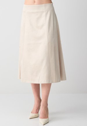 Jupe midi beige en ligne A portée avec des talons hauts assortis à bout pointu, vue de la taille aux pieds sur un fond neutre.