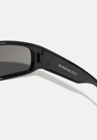 Lunettes de soleil noires avec une finition brillante, dotées de verres foncés, de branches droites et du logo "even&odd" sur le côté. Design minimaliste.