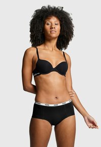 Schwarzer kabelloser BH mit geformten Cups und dünnen Trägern, kombiniert mit schwarzen Hipster-Unterhosen mit einem weißen Puma-Logo-Bund.