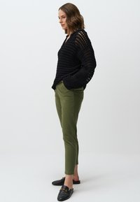 Maglione nero a maglia aperta con scollo a V, abbinato a pantaloni slim-fit verde oliva e mocassini neri con dettagli in metallo dorato.