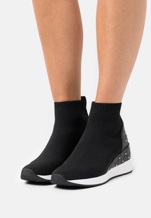 Schwarze, knöchelhohe Strickturnschuhe mit einer weißen Gummisohle und einem strukturierten Keilabsatz, der ein Diamantmuster und goldene Akzente aufweist.