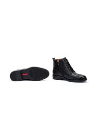 Bottines en cuir noir avec des détails en brogue, lacées sur le devant, fermeture éclair sur le côté, et semelle en caoutchouc texturée avec un accent rouge.