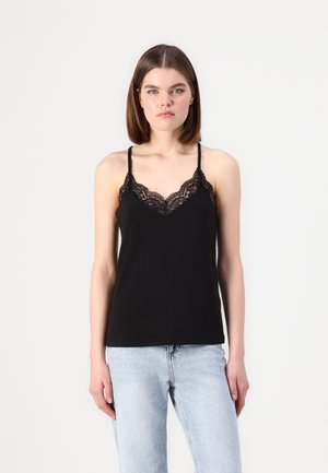 Zwarte camisole met kantdetails langs de halslijn, voorzien van dunne verstelbare banden en een relaxte pasvorm, gecombineerd met lichte spijkerbroek.
