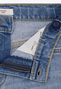 Szorty jeansowe o luźnym kroju; niebieskie z jasnym przetarciem, żółtym przeszyciem i zapięciem na dwa guziki. Posiadają metkę na pasku.