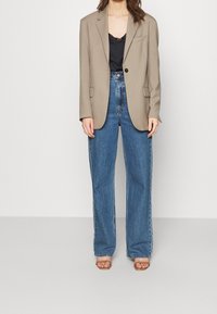 Beige tailored blazer with a single black button, paired with high-waisted blue denim jeans. The jeans are loose-fitting with a straight leg design.