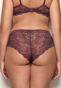 Reggiseno di pizzo viola e coordinato slip alti di pizzo indossati da una persona vista di spalle su uno sfondo neutro.