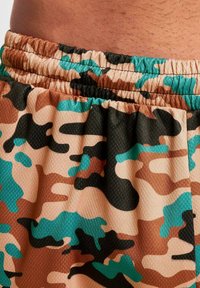 Kamuflasje svømmeshorts med en blanding av lysebrune, svarte og turkise mønstre. Elastisk midjebånd med samlet tekstur.