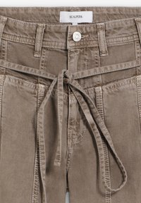 Pantalones marrones con cinturón de lazo frontal, botón de metal y etiqueta blanca visible con la marca "SCALPERS" en la cintura.