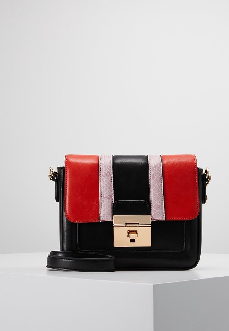 Bolso bandolera de cuero negro con acentos en rojo y rosa claro, herrajes dorados, cierre con hebilla plana y detalle de superficie texturizada.