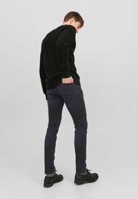 Svart stickad tröja med långa ärmar, kombinerad med mörka slim-fit jeans och svarta snörskor, sedd bakifrån. Minimalistisk design.