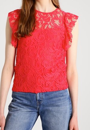 Top in pizzo corallo con un motivo floreale, maniche trasparenti e orlo ondulato abbinato a jeans azzurri chiari. Design texturizzato e fitted.