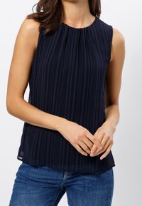 Mörkblå ärmlös topp med vertikala ränder, insamlad hals, mjuk tygkvalitet och avslappnad passform, bärs med denimjeans.